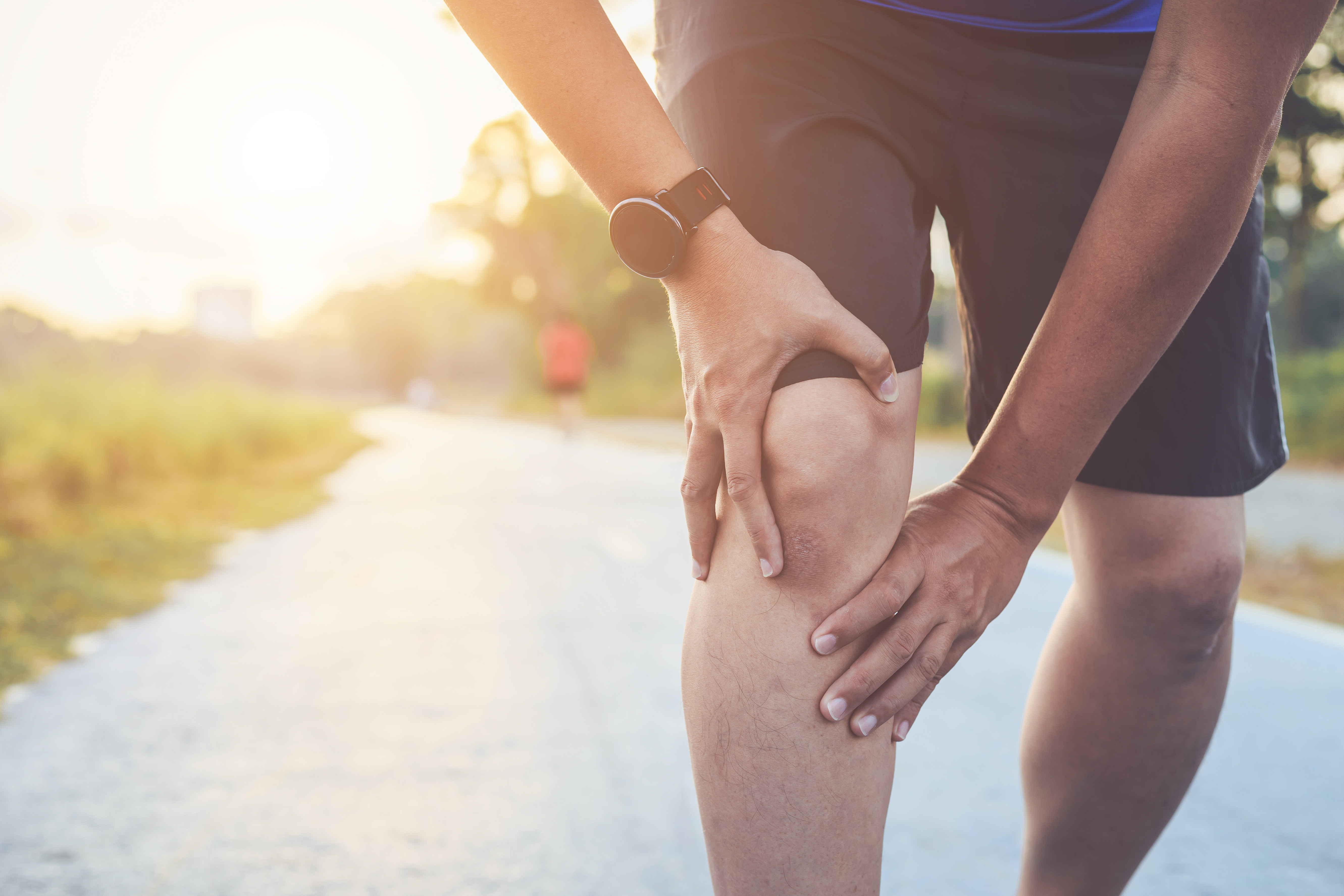 Man clutching his knee in pain while pausing during an outdoor run
