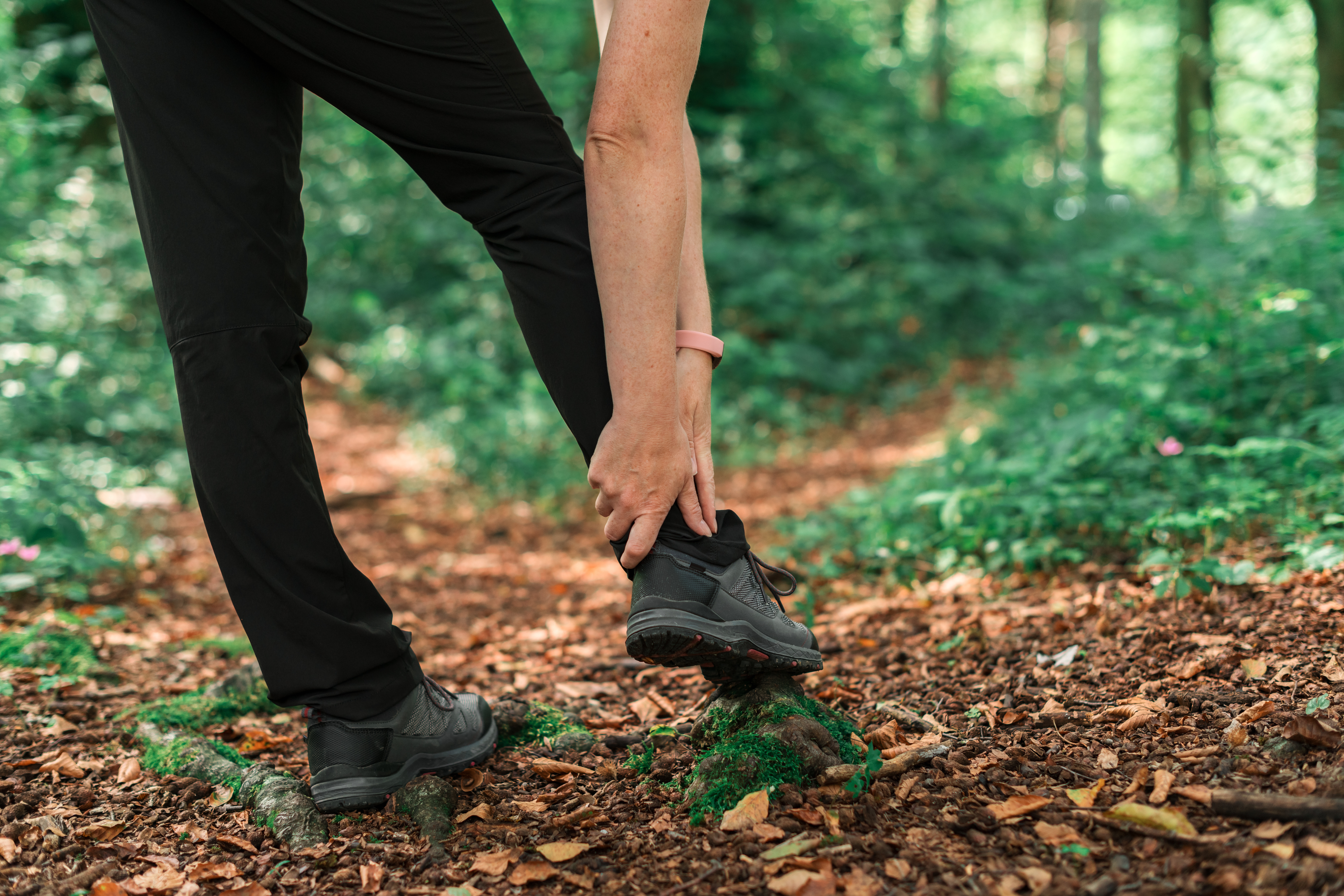 Hiker holding an injured ankle while pausing on a forest trail