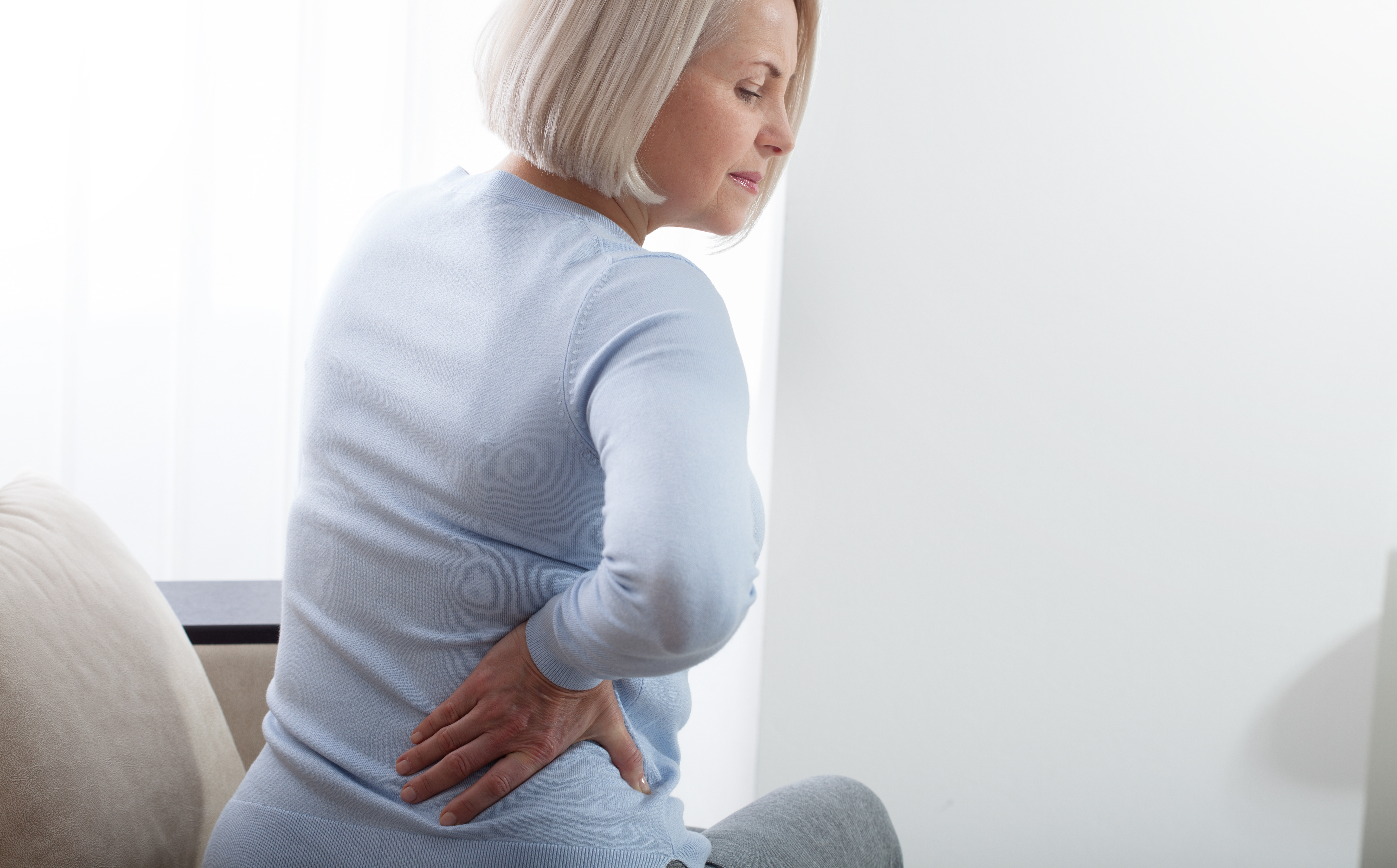 Woman sitting down and holding her lower back due to pain