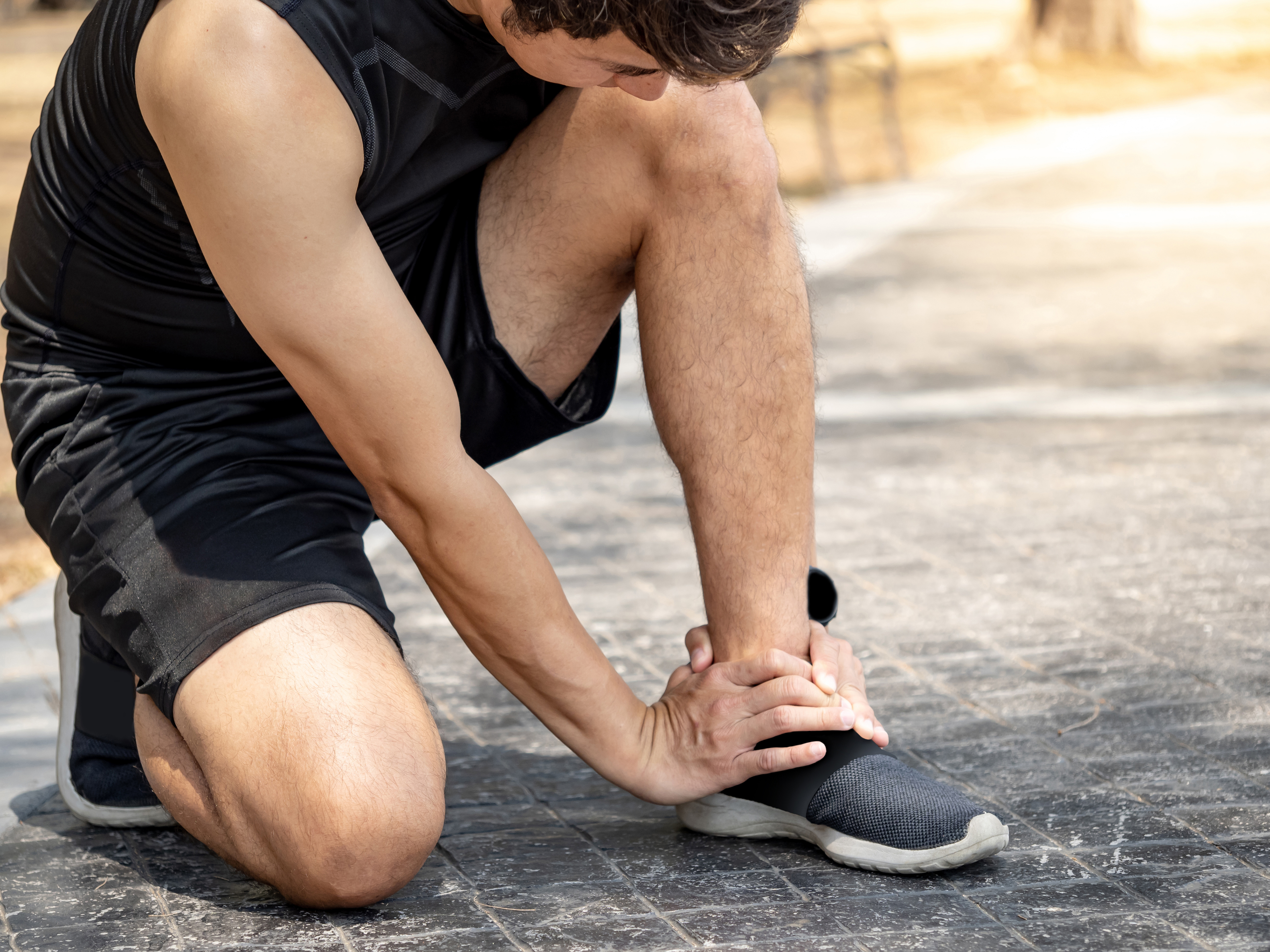 Man kneeling down and gripping his ankle in pain while on a run