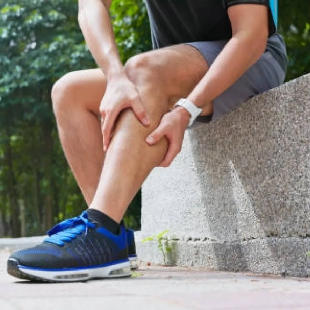 A young man is sitting down clenching his leg muscle after a long run.