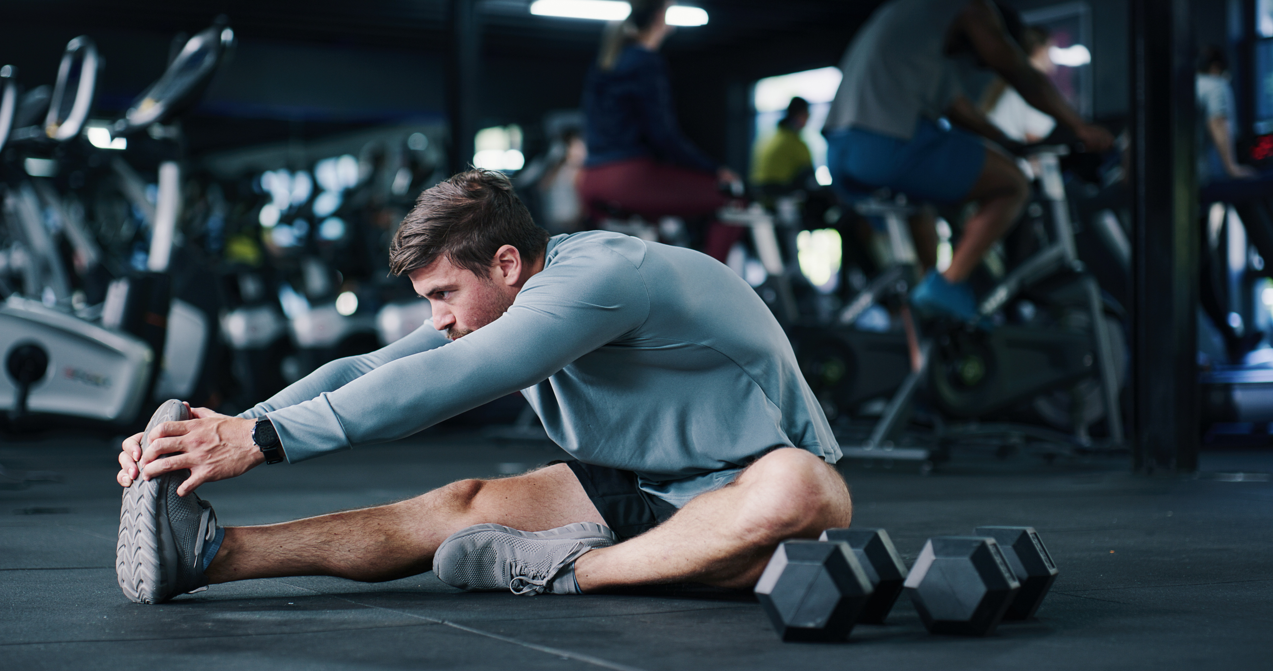 Man, stretching or gym with leg on floor for workout preparation, exercise or indoor training. Active, male person or getting ready with warm up or dumbbells for flexibility or fitness in health club.