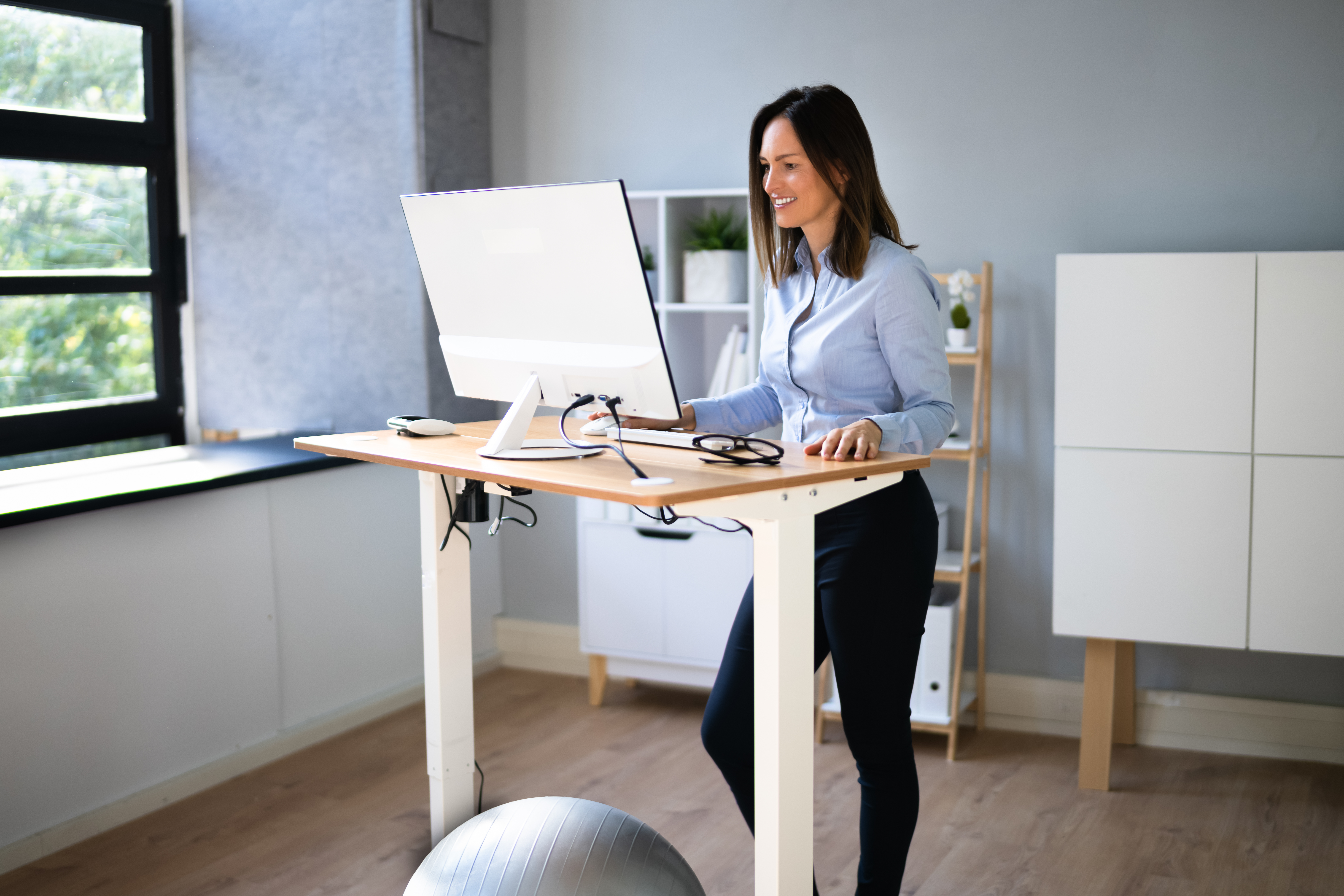 Woman Using Adjustable Height Standing Desk In Office For Good Posture
