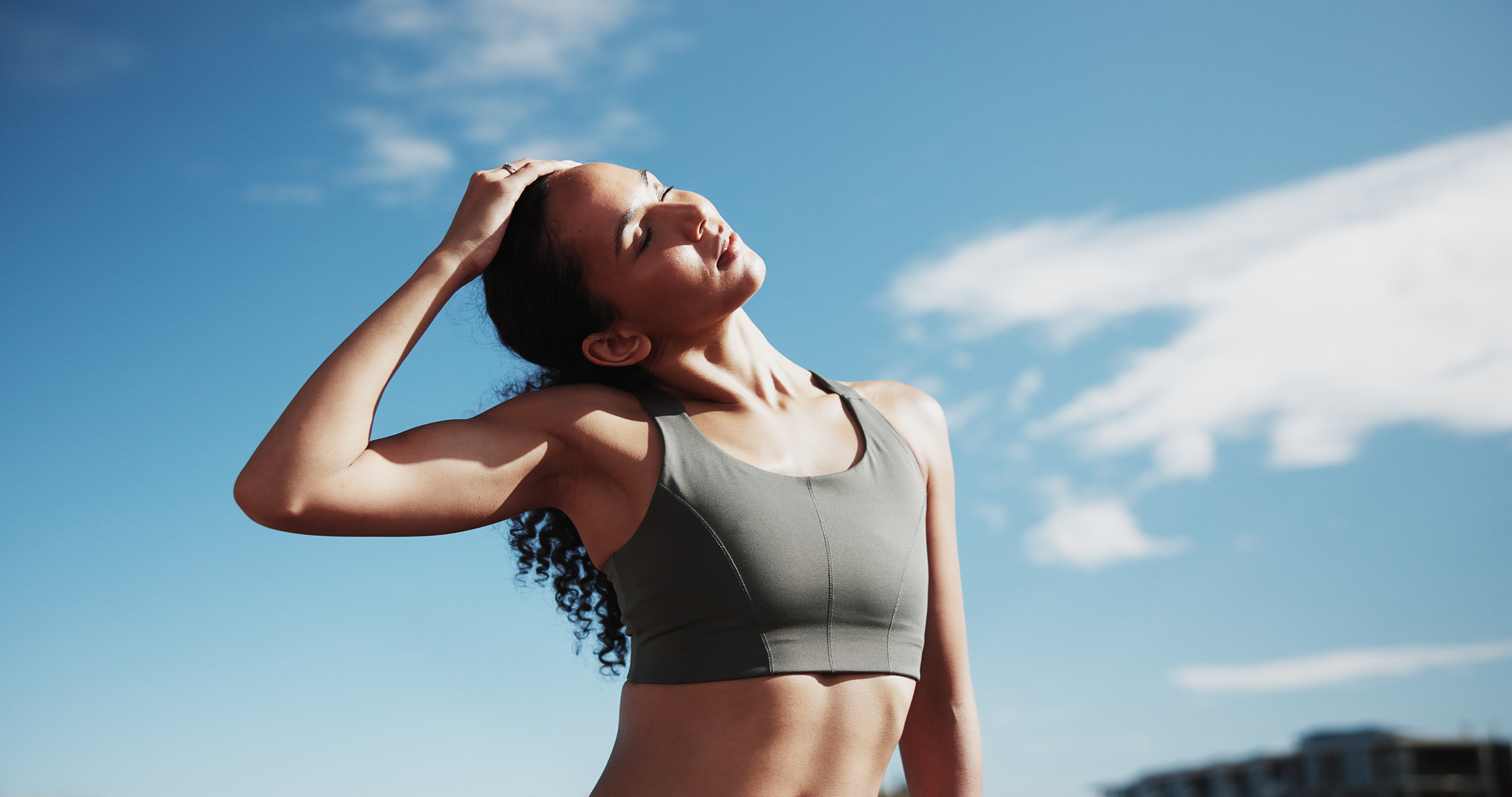 Fitness, city and woman stretching neck for exercise, training and warm up for workout with blue sky. Sports, runner and person getting ready for wellness, health or mobility for active hobby in town.