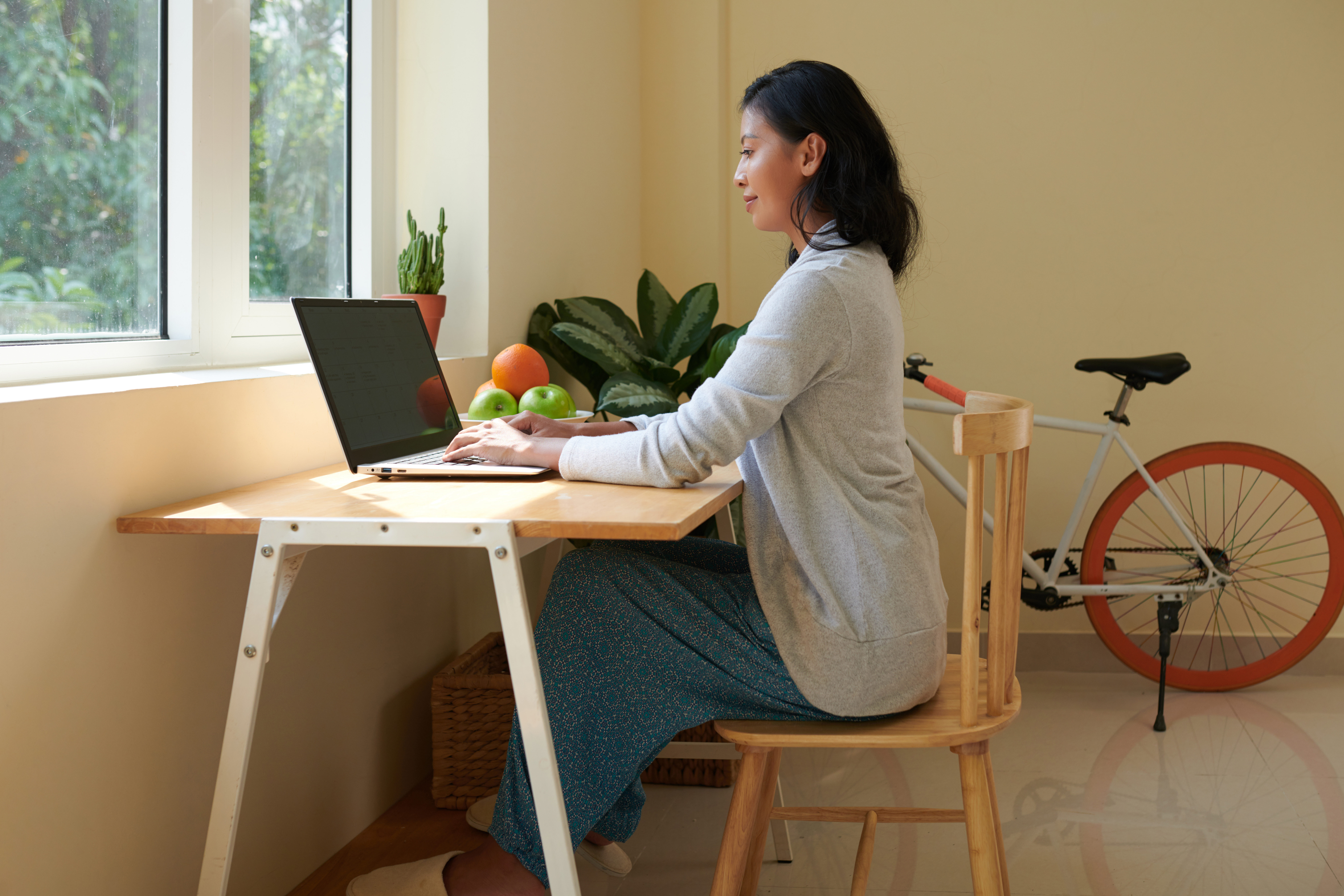 Smiling young woman with good posture wearing domestic clothes when working on laptop at home