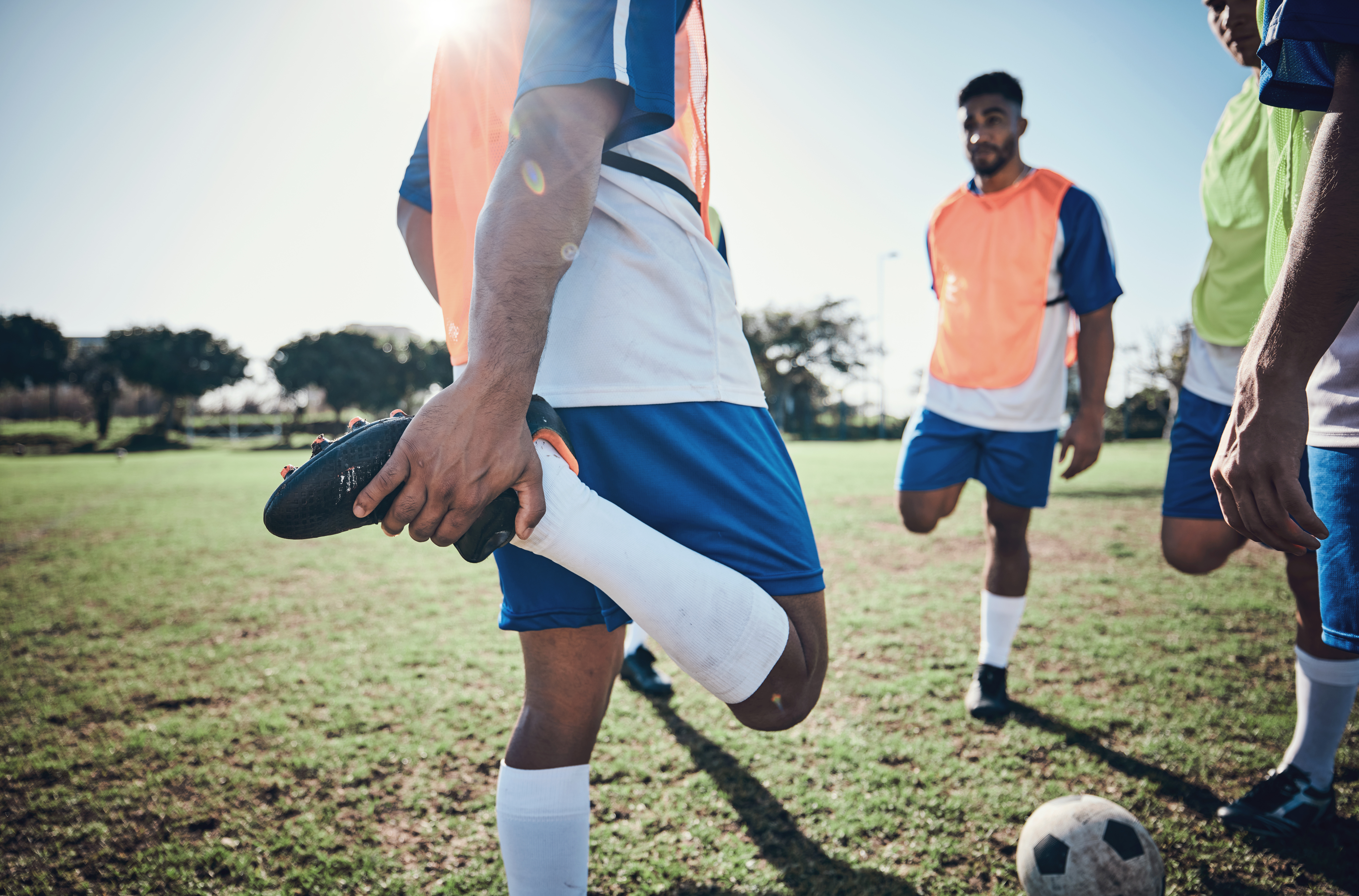 Football player, stretching legs and men training on a field for sports game and fitness. Male soccer team or athlete group outdoor for challenge, workout or warm up exercise on a grass pitch.
